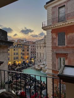 people are gathered on the balcony of an apartment building overlooking a pool and fountain at sunset