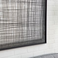 a black and white painting hanging on the wall next to a gray couch in front of a brick wall