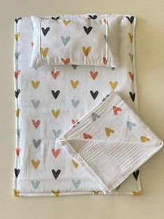 a white blanket with hearts on it next to two folded napkins and a pillow