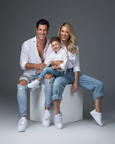 a man and woman sitting on top of a white box holding a small child in their lap