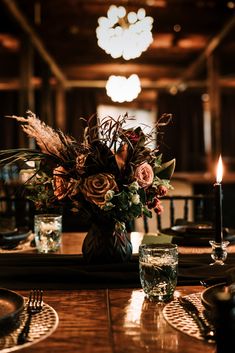 a wooden table topped with a vase filled with flowers next to two glasses and a candle