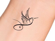 a small bird tattoo on the back of a woman's arm, with black ink