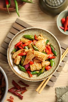 a bowl filled with chicken and vegetables next to chopsticks on a wooden table