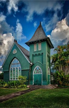 a green church with a steeple and stained glass windows on the front door is surrounded by palm trees