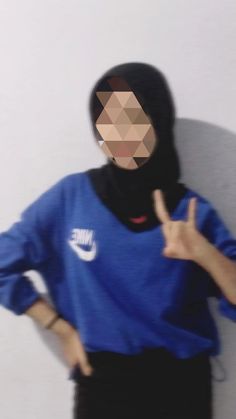 a woman wearing a blue shirt and black pants is making the peace sign with her hands