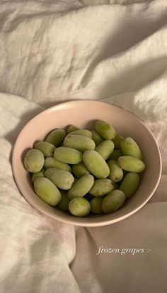 a bowl filled with green beans sitting on top of a white bed cover covered in sheets