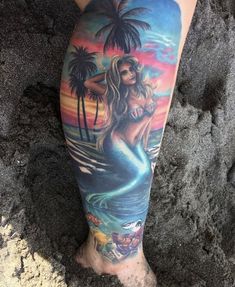 a woman's leg with a mermaid tattoo on it and palm trees in the background