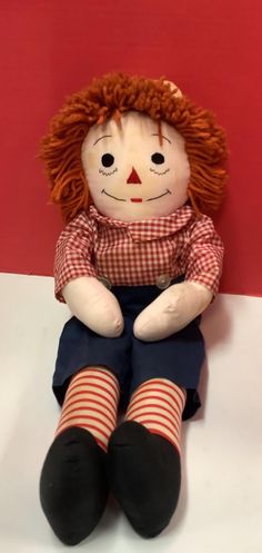 a doll with red hair sitting on top of a white table next to a red wall