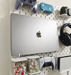 an apple computer sitting on top of a white wall next to video game remotes