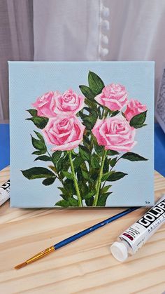 a painting of pink roses on a blue background next to some markers and paintbrushes