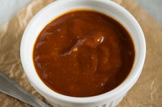 a white bowl filled with sauce sitting on top of a piece of wax paper next to a spoon