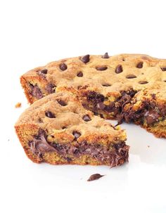 a chocolate chip cookie cake cut in half on a white surface with one piece missing