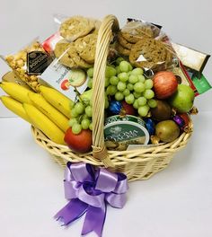 a wicker basket filled with assorted fruit and snacks next to a purple ribbon