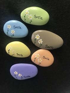 four painted rocks with flowers and the words smile, smile, smile