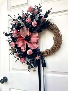 a wreath with pink and black flowers hanging on the front door to a white door