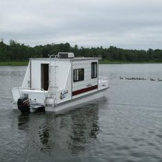 a houseboat floating on top of a lake with ducks swimming in the water behind it