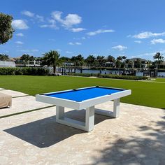 a blue pool table sitting on top of a cement floor next to a lush green field