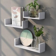 two white floating shelves with plants and books on them, against a gray wall background