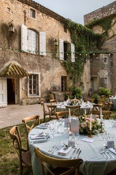 an outdoor dining area with tables and chairs in front of a stone building that has ivy growing on it