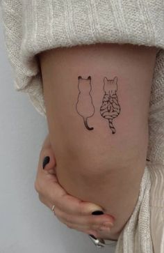 a woman's thigh with two cats tattoo on her stomach and one cat sitting next to the other