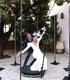 a bride and groom dancing on a trampoline in front of a tree at their wedding