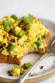 a white plate topped with a piece of bread covered in green vegetables next to a fork