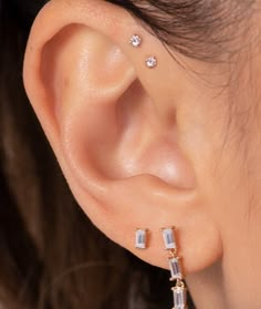 a close up of a person's ear with two small diamond earrings on it