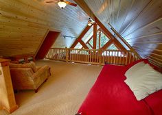 an attic bedroom with red bedding and wooden walls, along with two chairs on either side