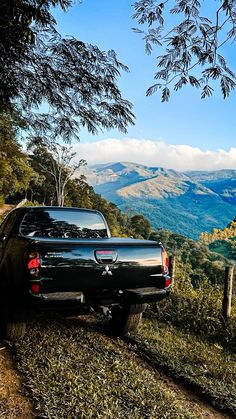 a black truck parked on the side of a dirt road next to a lush green hillside