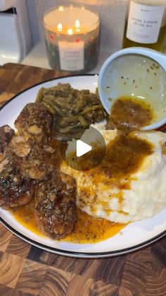 a plate with mashed potatoes, meat and gravy next to a candle