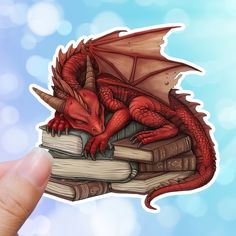 a red dragon sitting on top of a pile of books with its wings spread out