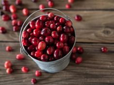 a bucket filled with cranberries on top of a wooden table