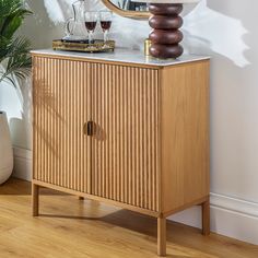 a wooden cabinet with a mirror and two wine glasses on top of it next to a potted plant