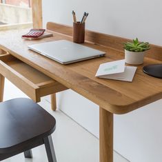 a laptop computer sitting on top of a wooden desk next to a plant and chair