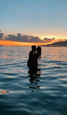 two people are kissing in the water at sunset, with an island in the background