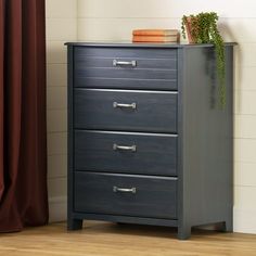 a black dresser with three drawers in front of a curtained wall and wooden floor