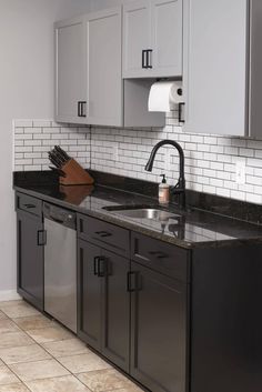 a kitchen with black counter tops and gray cabinets, white subway backsplashes