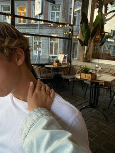 a young man is holding his hand to his neck while sitting at an outdoor cafe