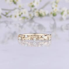 a gold wedding band with leaves and diamonds on it, sitting in front of white flowers