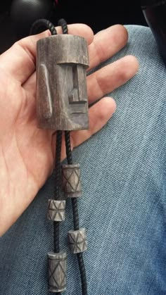 a person is holding a necklace made out of wood and metal beads on a black cord