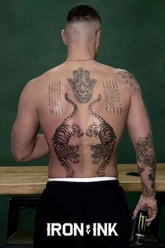 a man with tattoos on his back holding a beer in front of a chalkboard