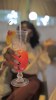 a woman holding up a glass with a drink in it on top of a table