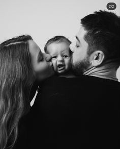 a black and white photo of a man kissing a woman's face as she kisses her baby