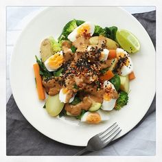 a white plate topped with meat, veggies and hard boiled eggs next to a fork