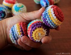 a hand holding small crocheted balls on top of a wooden table