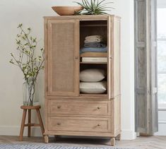 a wooden cabinet filled with lots of pillows and blankets next to a potted plant