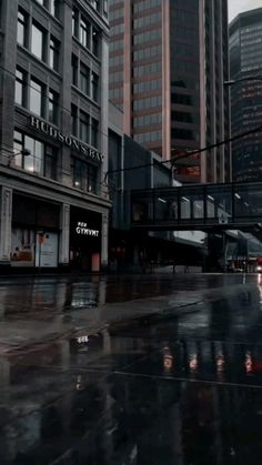 an empty city street in the rain with tall buildings on either side and one person holding an umbrella