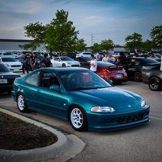 a blue car parked in a parking lot next to other cars and people standing around