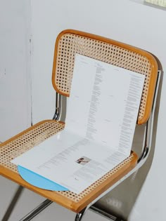 an open book sitting on top of a wooden chair next to a metal frame and white wall