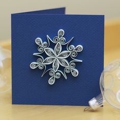 a blue card with an intricate snowflake design on the front and back, sitting next to a christmas ornament